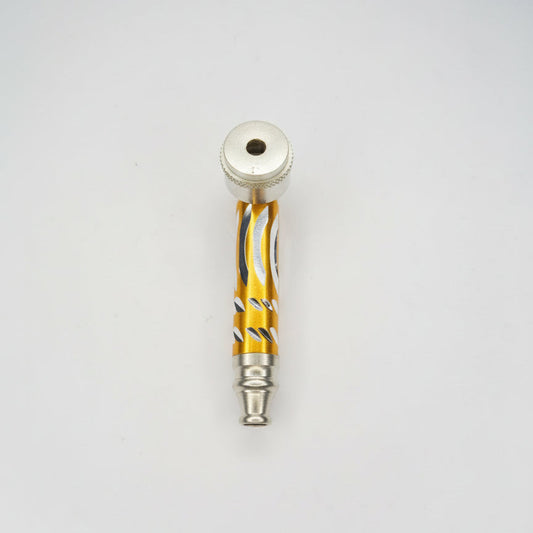 Gold-tone metal hand pipe with cutout-pattern stem and silver-tone bowl, compact smoking accessory on a light background