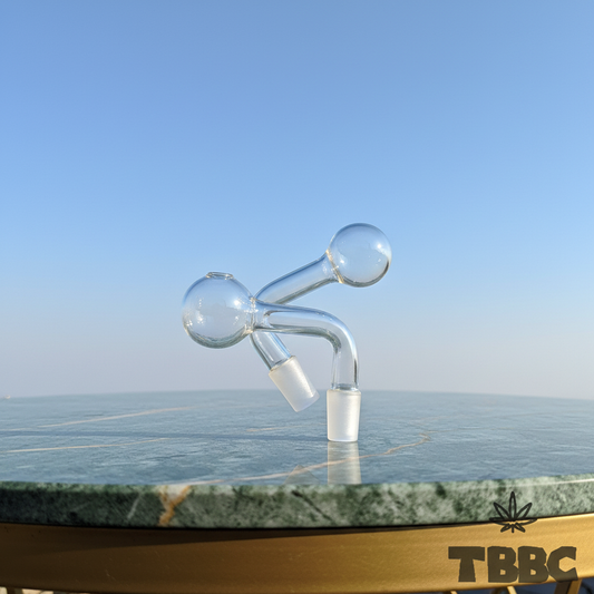 Two clear glass oil pipe attachments with curved necks and 14mm male joints on marble with a sky background
