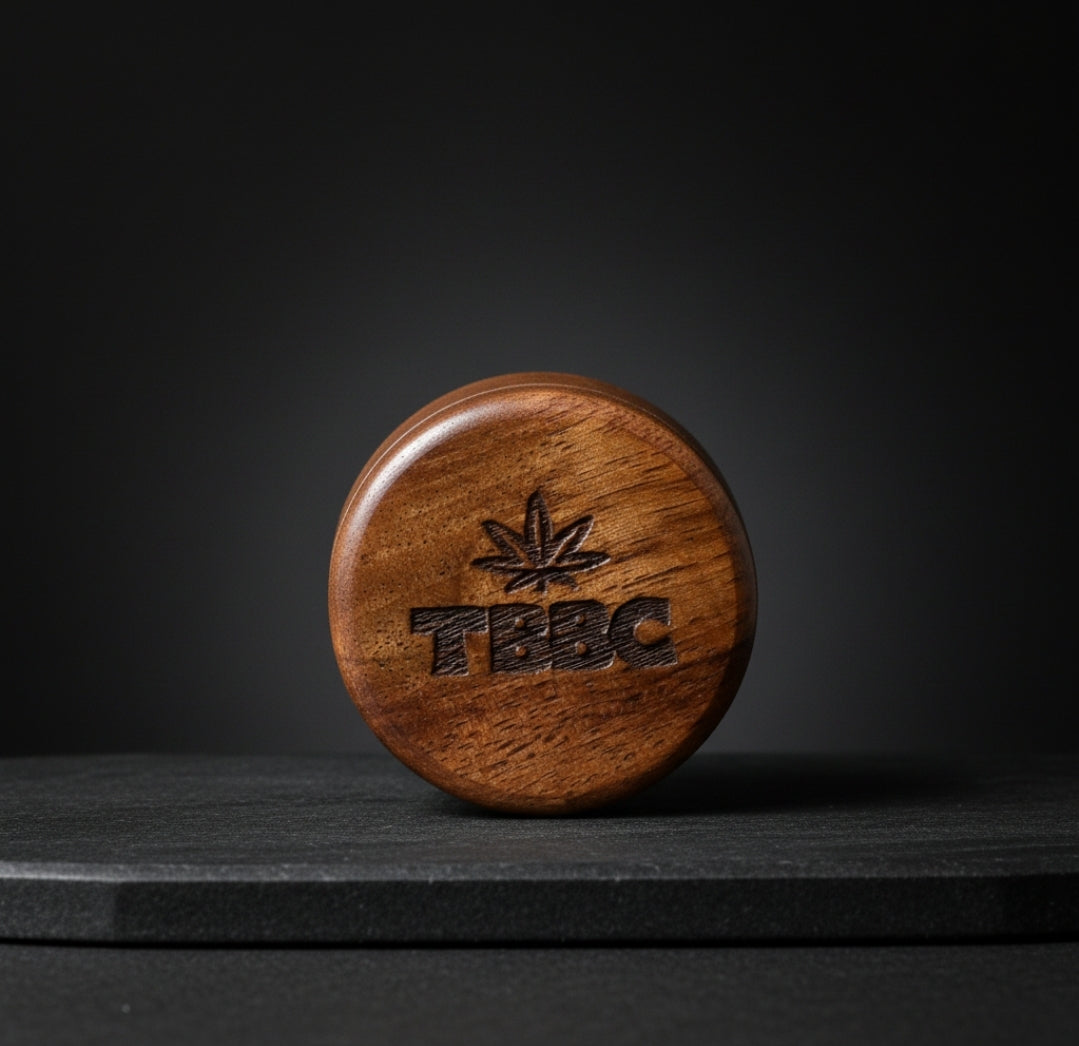 TBBC Signature 56mm wooden herb grinder closed to show the engraved lid and natural wood grain against a dark backdrop.