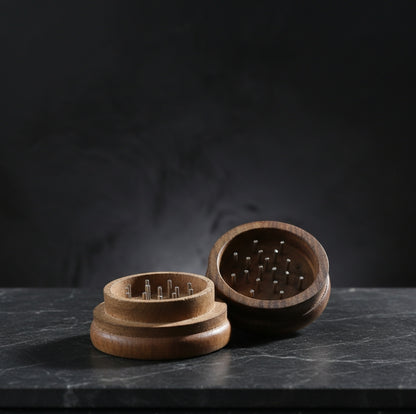 Open TBBC Signature 56mm wooden herb grinder showing the interior chamber and grinding pegs against a dark backdrop.