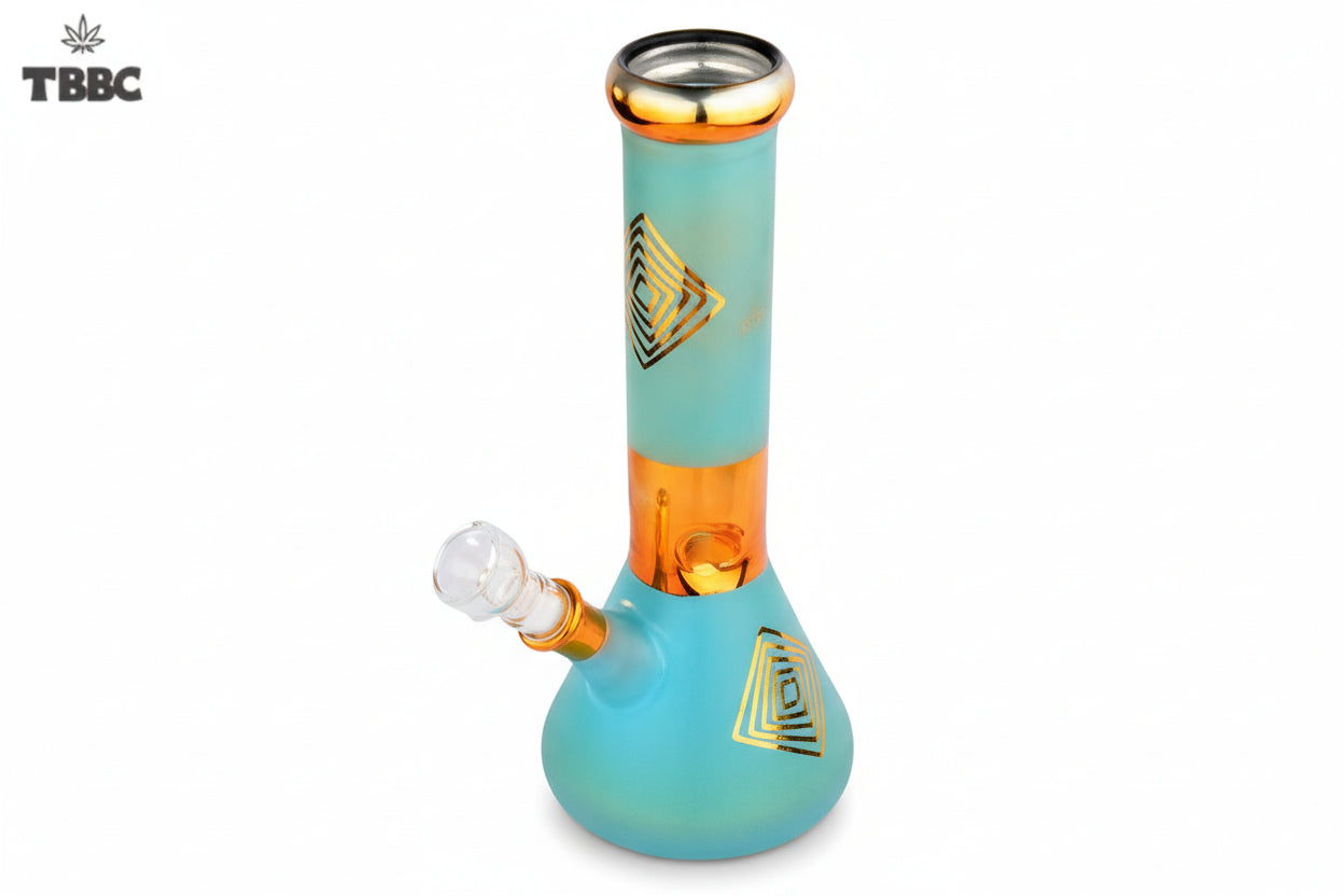 A blue glass bong with gold accents and geometric patterns, featuring a thick base and a narrow top, with a small amount of white smoke rising from the top. 