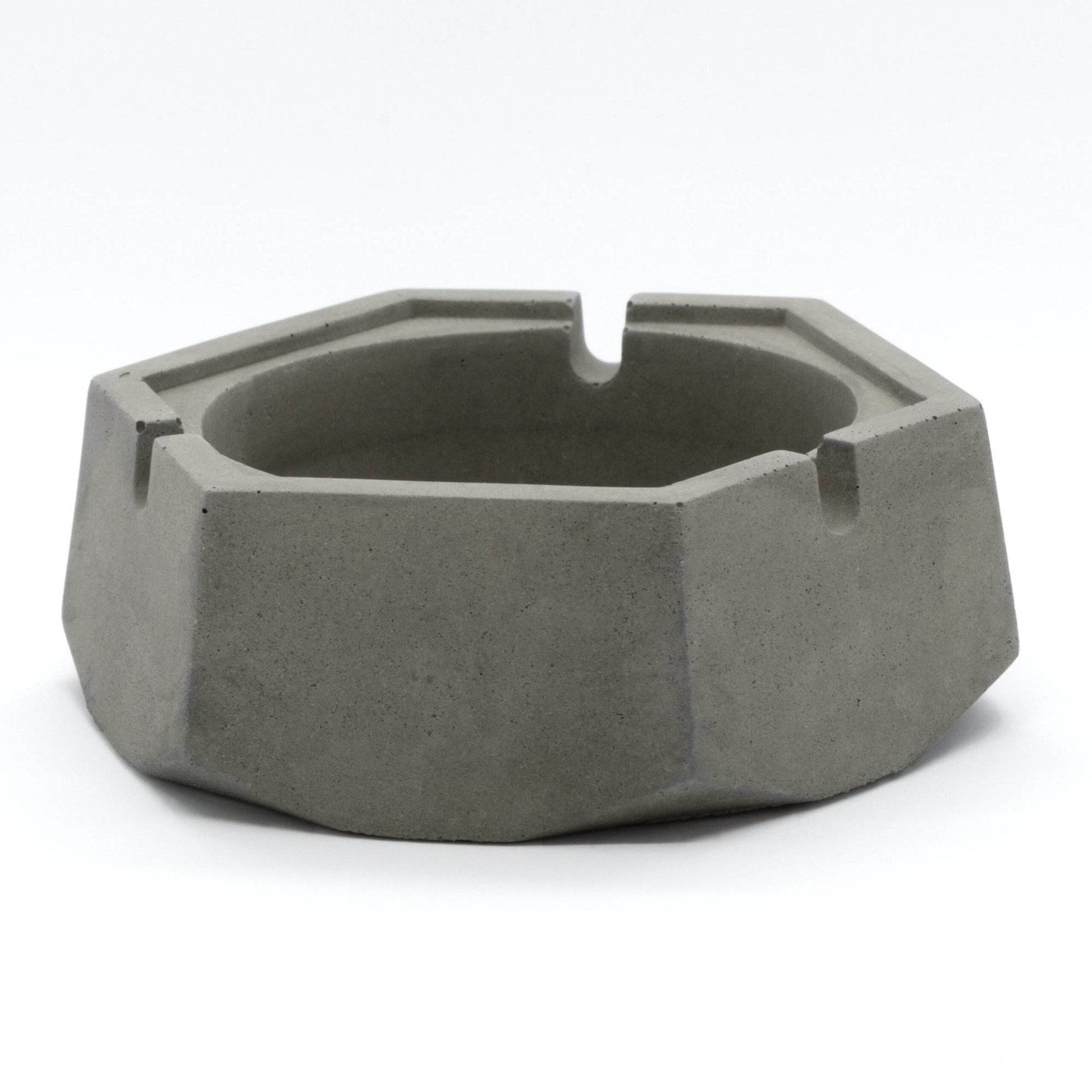 A dark, concrete ashtray with a geometric hexagonal shape, featuring a smoker holding a cigarette.hexagon greyt dankest stoner ashtrays, cement handcrafted home decor lifestyle ashtray,best cigarette_ashtray online nearby instant delivery