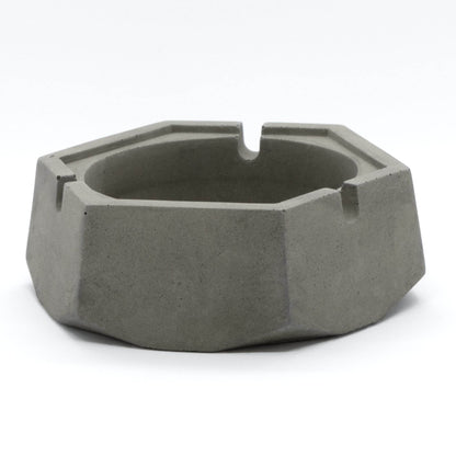 A dark, concrete ashtray with a geometric hexagonal shape, featuring a smoker holding a cigarette.hexagon greyt dankest stoner ashtrays, cement handcrafted home decor lifestyle ashtray,best cigarette_ashtray online nearby instant delivery