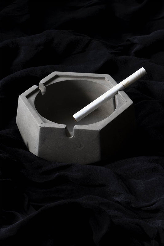 A dark, concrete ashtray with a geometric hexagonal shape, featuring a smoker holding a cigarette.hexagon greyt dankest stoner ashtrays, cement handcrafted home decor lifestyle ashtray