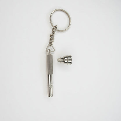 Metal keychain with a small attached component on a light gray, Metal key-shaped keychain on a plain background. Metal keychain with a tool-like design on a light gray background, small toking weed hand pipe key chain, easy to carry smoking accessory online instant delivery, best one hitter for weed stoners 420 lifestyle peace. tbbc, one hitter for weed  background