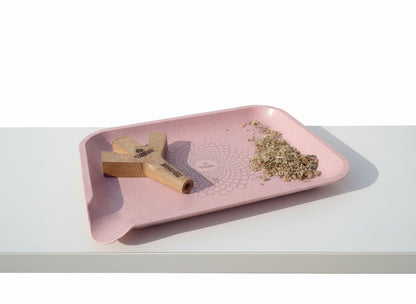 Pink tray with trident joint holder, rolled joint, and herbal mixture buds on a tbbc rose pink rolling tray