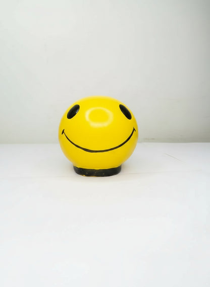 Yellow ball with a smiley face design attached to a white wall.
